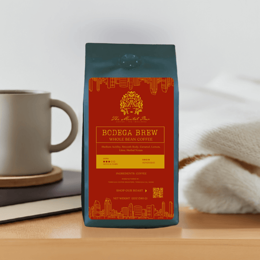 A packaged bag of Bodega Brew coffee on a table with a cup of coffee and a sweater in the background.