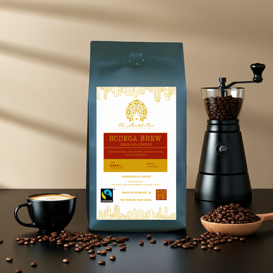 Bodega Brew Fair Trade Honduras medium roast coffee bag with a manual grinder, cappuccino, and roasted coffee beans on a dark surface.